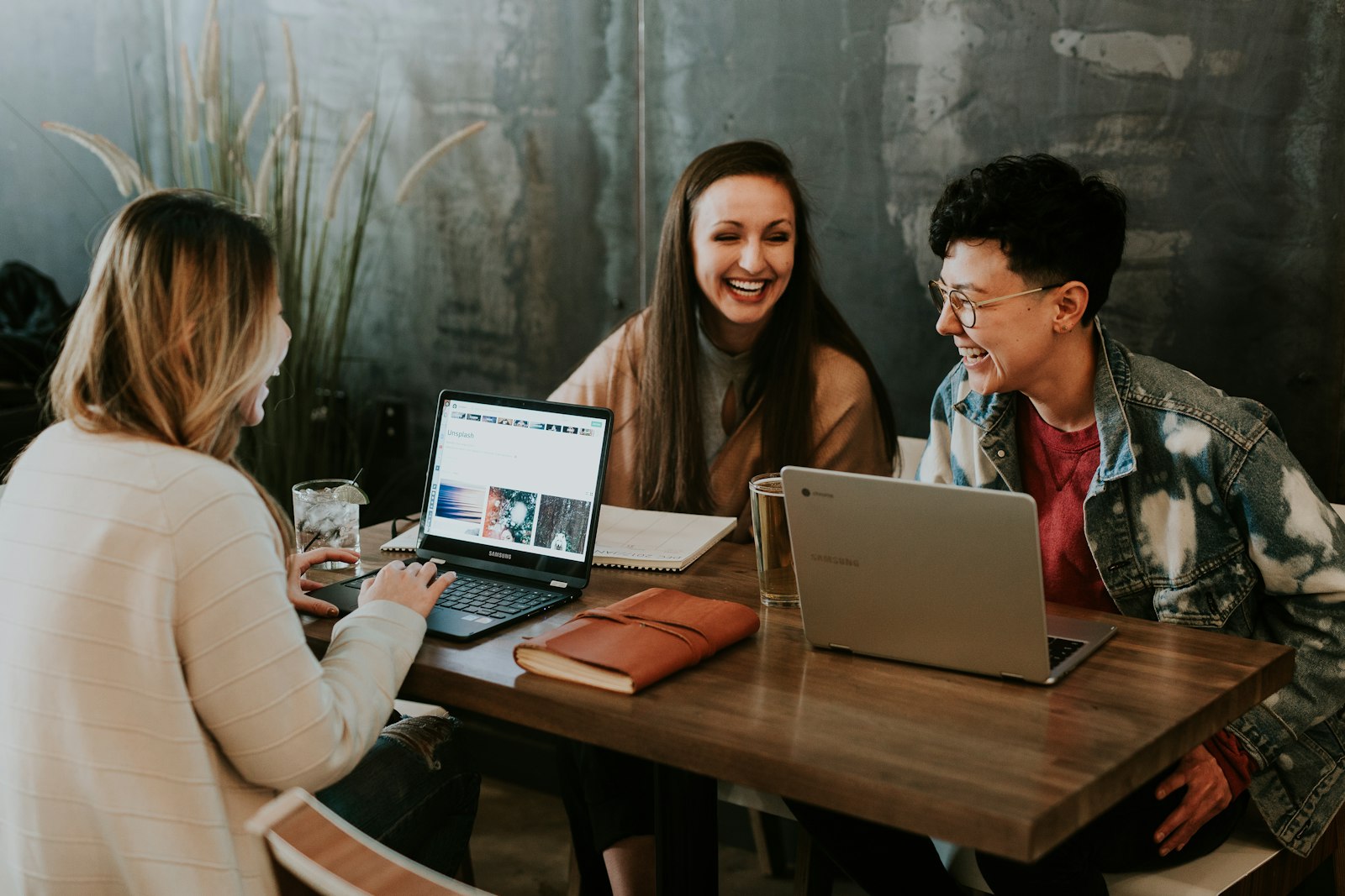 Drei Personen lachen bei der gemeinsamen Arbeit am Laptop